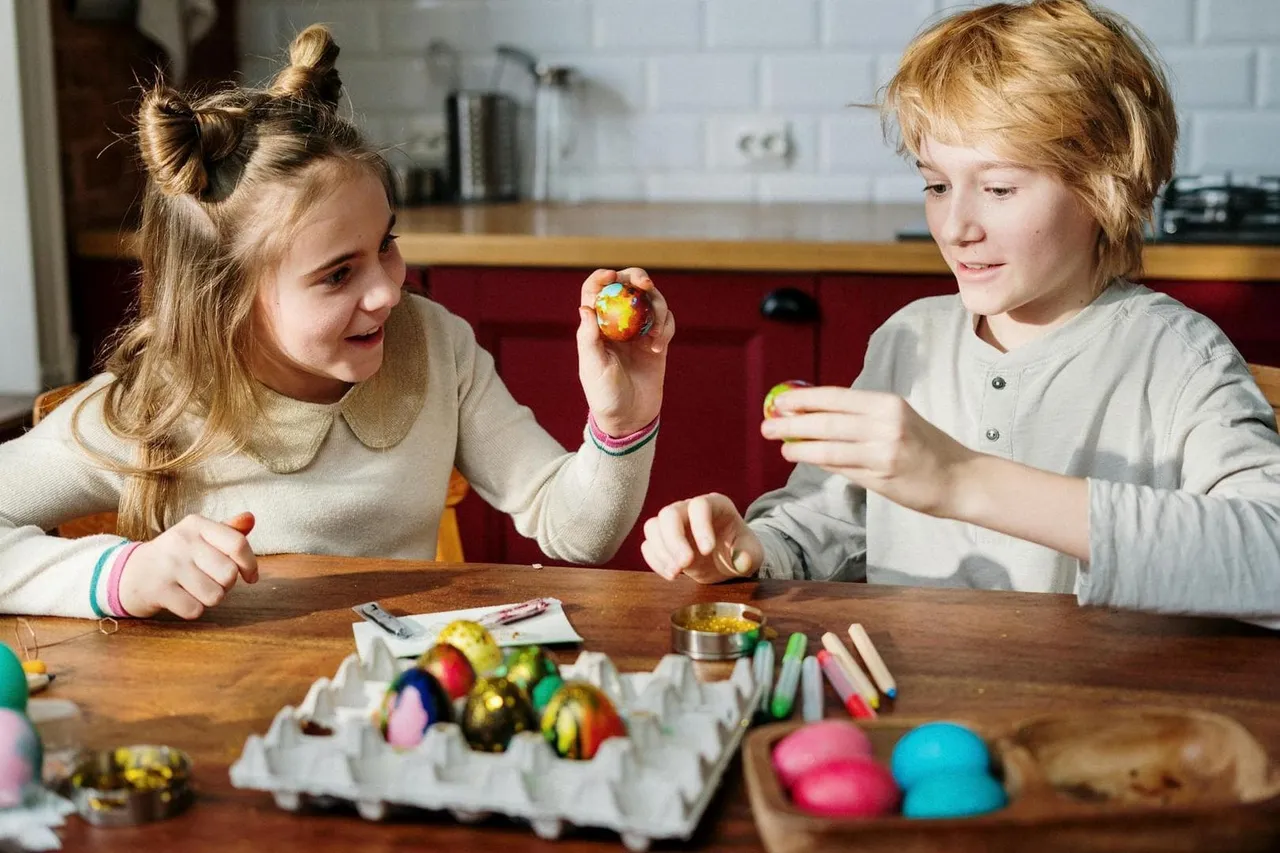 Zwei Kinder dekorieren bunte Ostereier am Tisch mit verschiedenen Bastelmaterialien