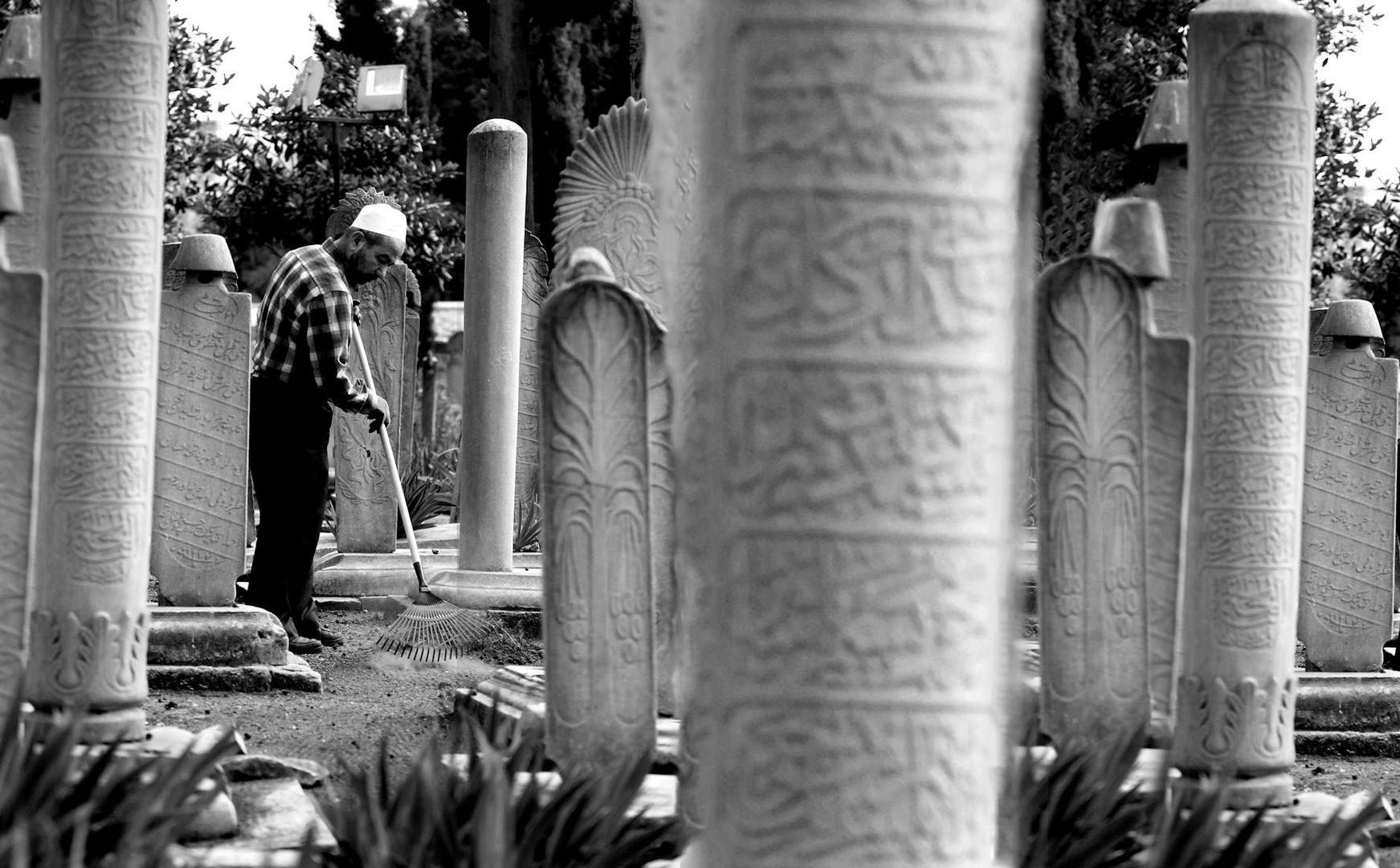 Mann harkt Laub zwischen historischen Grabsteinen auf einem Friedhof