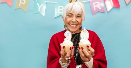 Lächelnde ältere Frau hält Cupcakes mit Kerzen bei Geburtstagsfeier