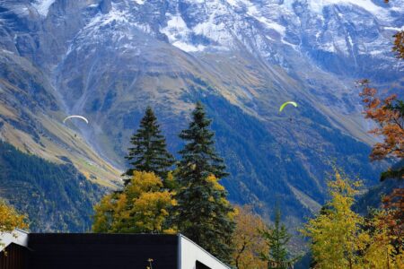 Zwei Gleitschirmpiloten fliegen über eine Berglandschaft mit schneebedeckten Gipfeln